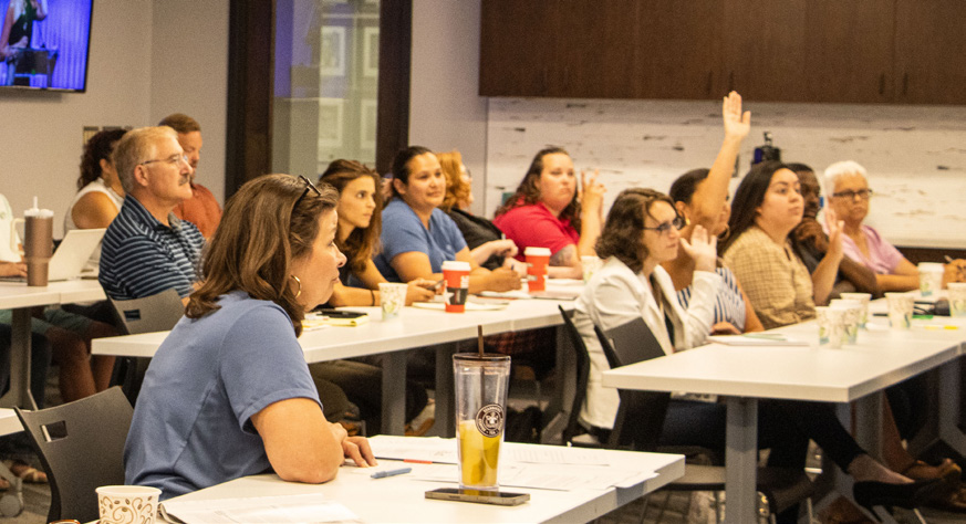 Training attendees seated in a classroom, with one participant raising a hand